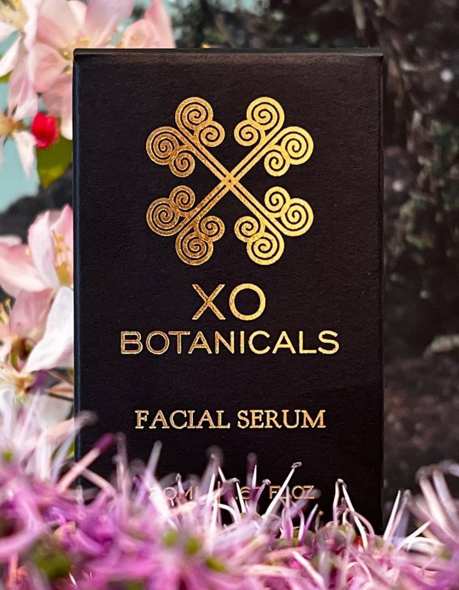 XO Facial Serum box with the gold XO knot, among pink blossoms